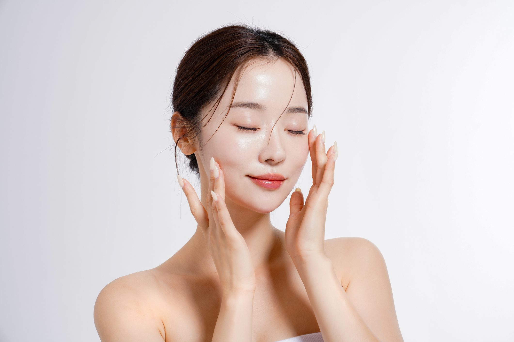 A woman gently applying skincare cream to her face with closed eyes.
