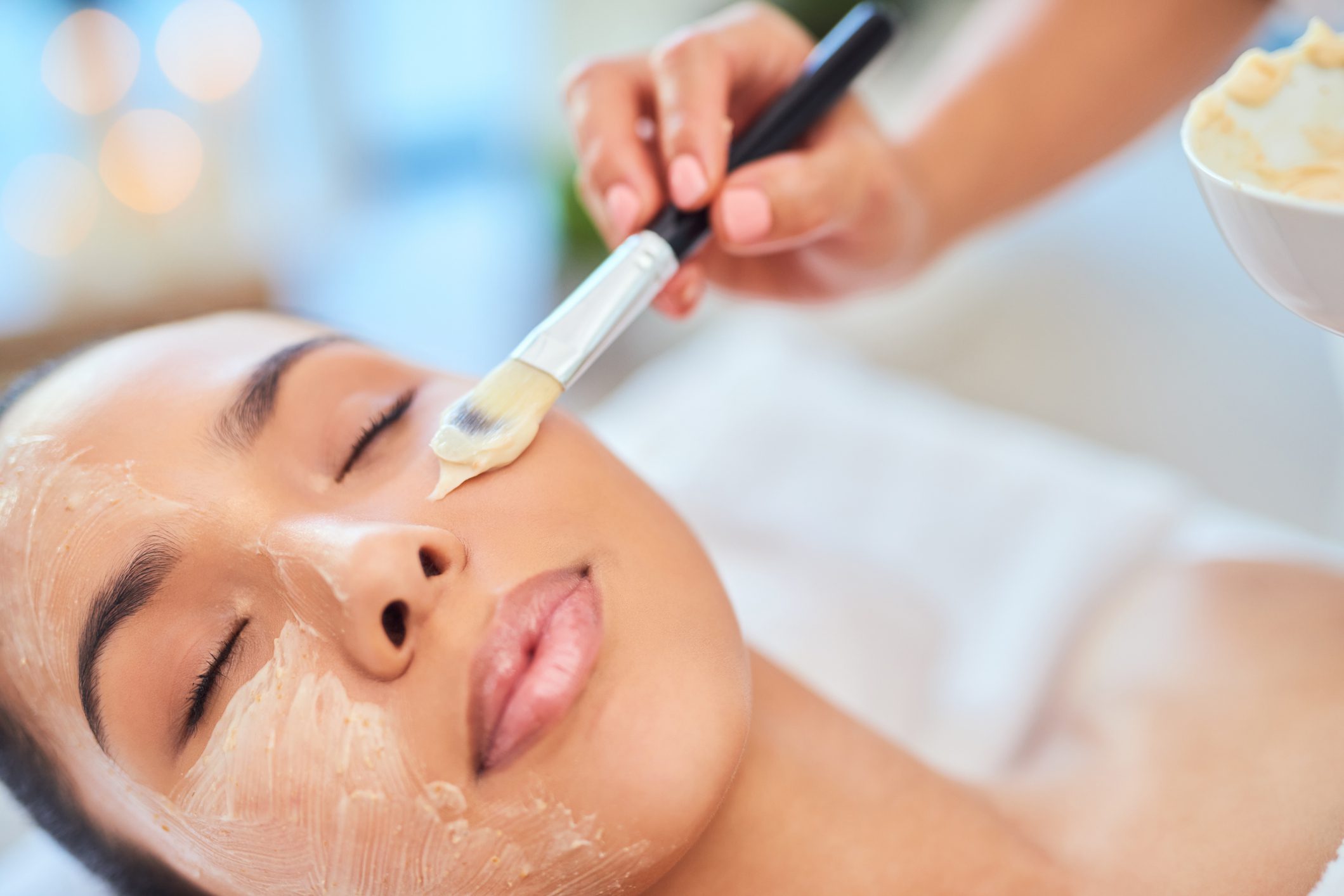 A woman receiving a facial treatment with a brush applicator.